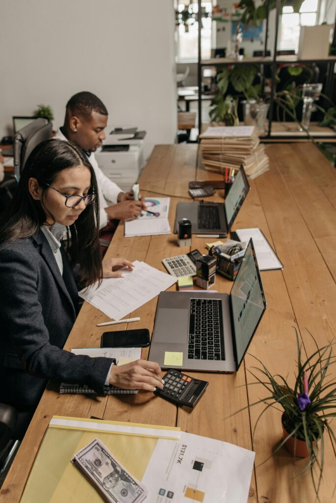 Small business professionals reviewing financial documents and bookkeeping reports while working on laptops in an office