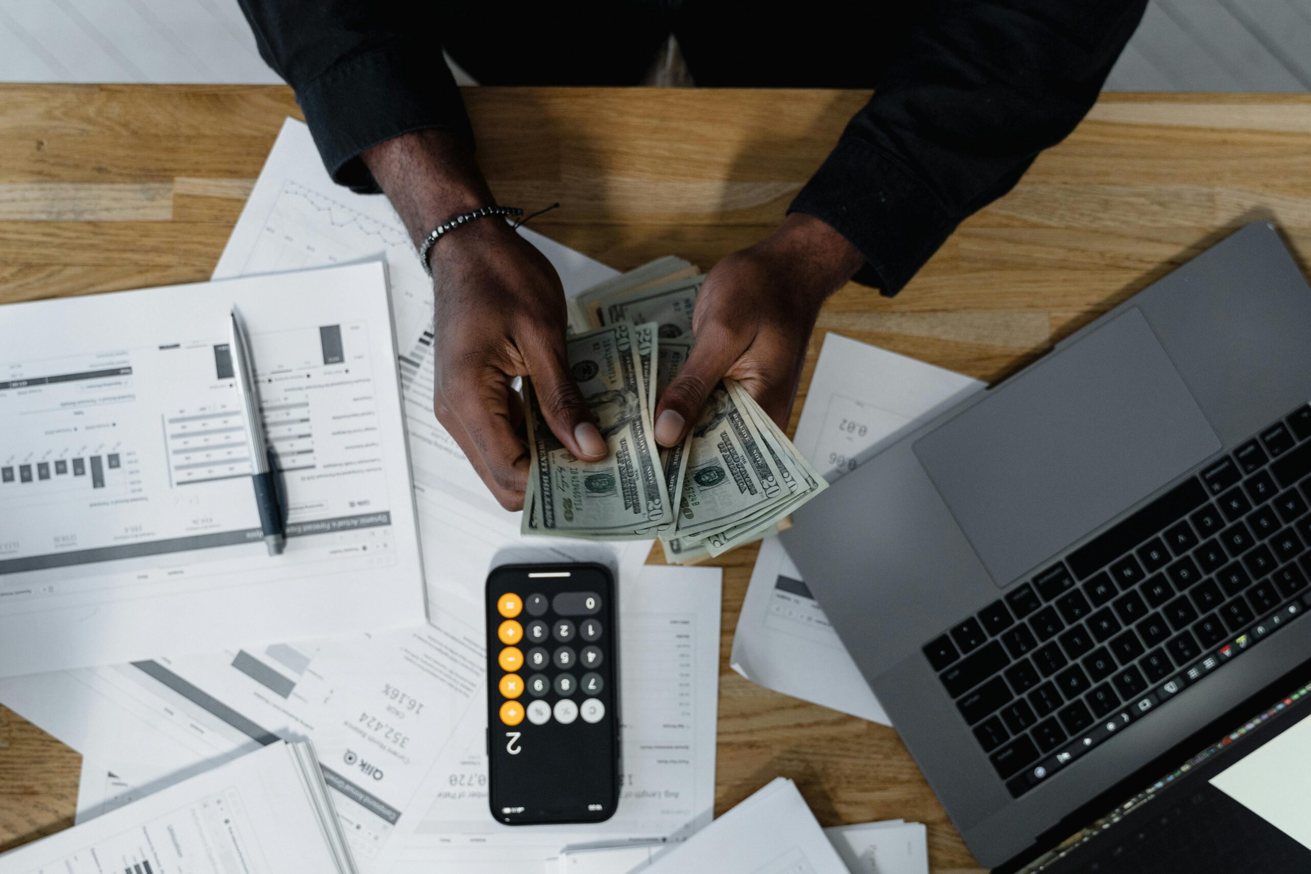 Small business owner reviewing cash and financial documents next to a laptop and calculator during bookkeeping reconciliation